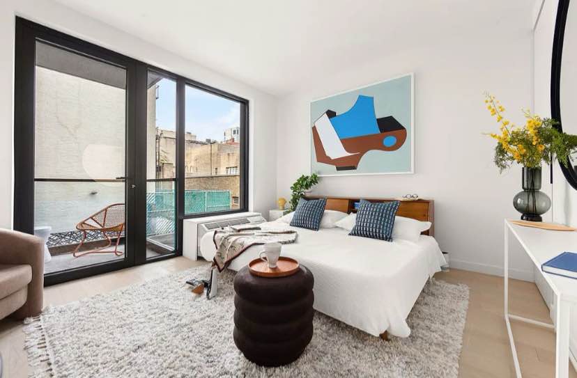 The home begins with a spacious living, dining, and sleeping area saturated with natural light. The living area leads out onto the balcony, while the kitchen is equipped with a sleek Italian Marmi Scala terrazzo countertop, chic Newform fixture, custom Alta Cucine cabinets, a Falmec Virgola recirculating hood, and a suite of high-end Bertazzoni and Blomberg appliances.