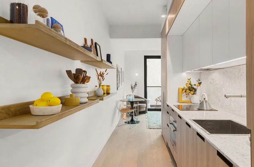 The home begins with a spacious living, dining, and sleeping area saturated with natural light. The living area leads out onto the balcony, while the kitchen is equipped with a sleek Italian Marmi Scala terrazzo countertop, chic Newform fixture, custom Alta Cucine cabinets, a Falmec Virgola recirculating hood, and a suite of high-end Bertazzoni and Blomberg appliances.