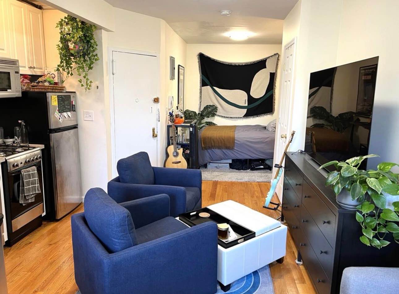 I'm looking for a chill individuals to lease my apartment! This is a well-designed studio with an open layout that feels bigger than it is, thanks to the hardwood floors and lots of natural light. The main area is set up with a comfy living space (those two blue armchairs are perfect for relaxing!) and a dedicated spot for eating or working by the window. The kitchen is tucked away and features white cabinets, a microwave, a small gas stove, and a dishwasher. You'll also find great storage space, including a closet with built-in organization for clothes and shoes. The whole place is decorated with a modern, lived-in style that includes my big TV, musical instruments, and cool wall art. It's a comfortable and functional home in a super central location, and I'm looking for someone tidy and respectful to share it with! Send me a message and tell me a bit about yourself!